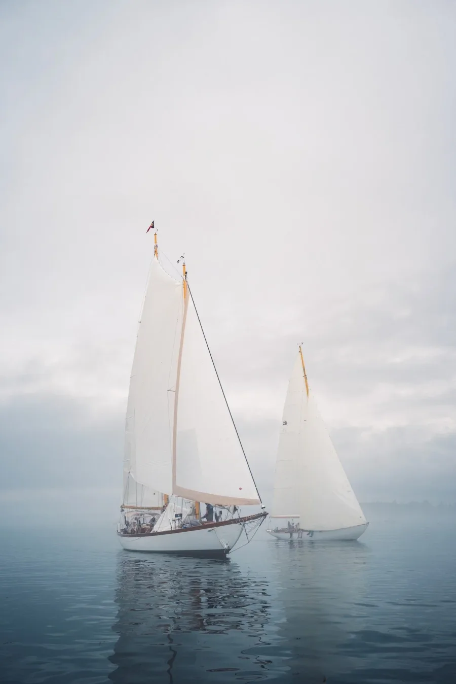 A white sailboat reflected in still, misty water