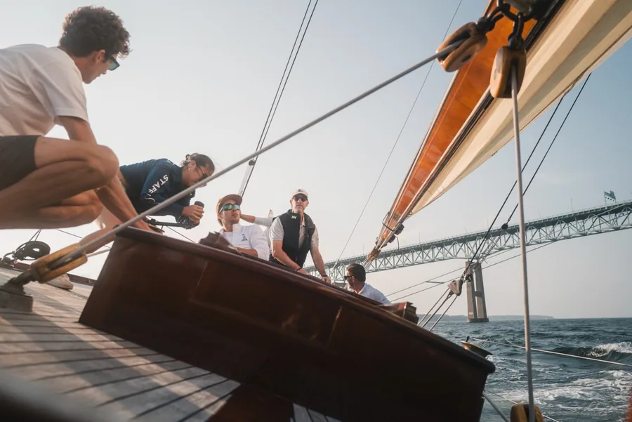 Crew aboard a wooden sailboat on the water.